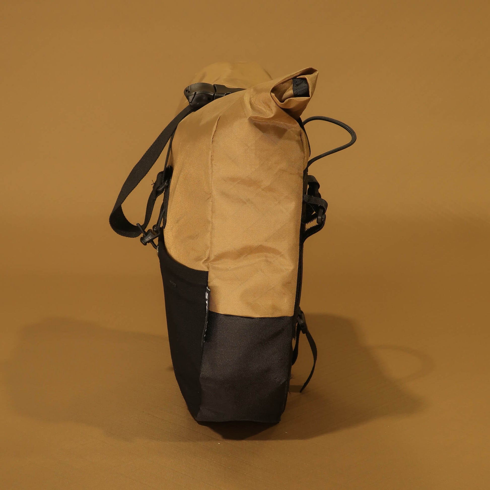 Side profile of 8L Coyote pannier showing tapered shape, coyote tan upper and black lower panels, side zip pocket, and stretch pocket