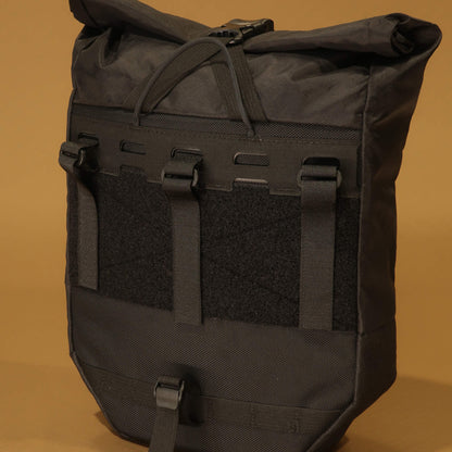 Close-up detail of the 10L black pannier's rear rack attachment system showing straps, velcro panel, and buckle clips
