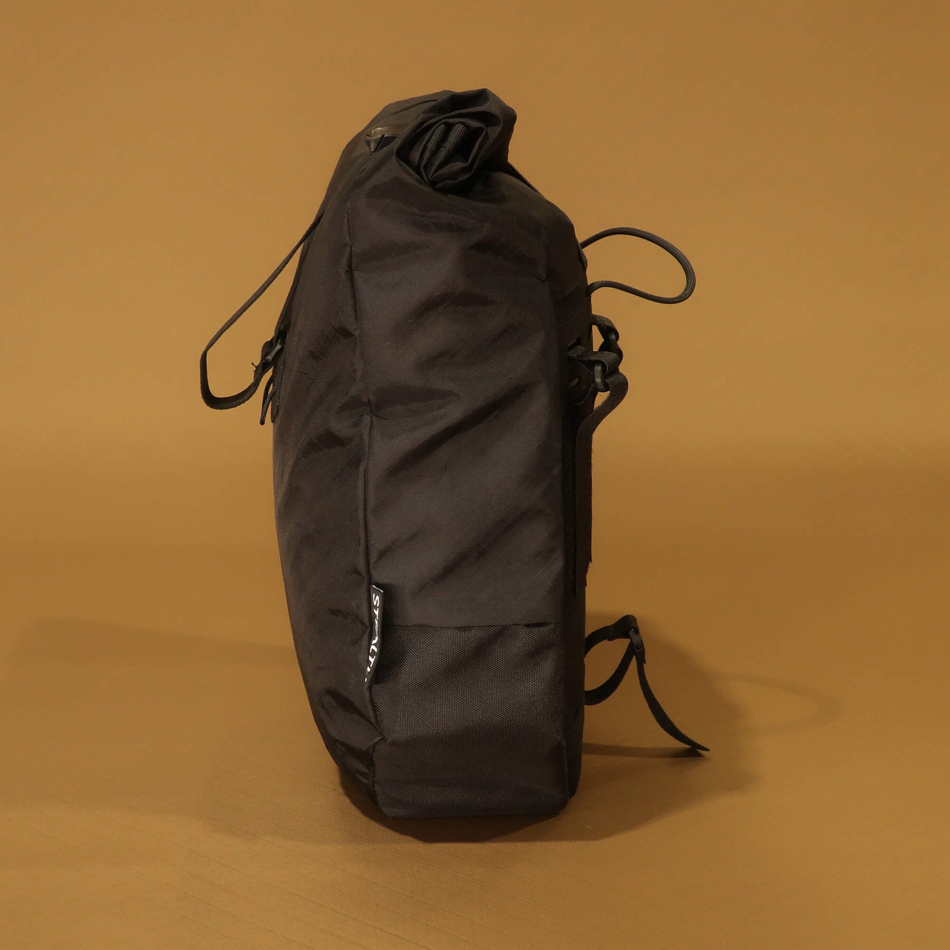 Side profile of black 10L roll-top bicycle pannier showing rounded tapered shape and side zip pocket
