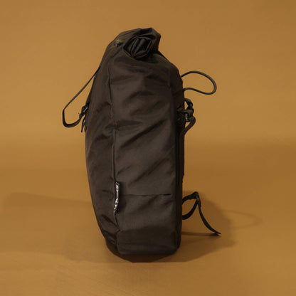Side profile of black 10L roll-top bicycle pannier showing rounded tapered shape and side zip pocket