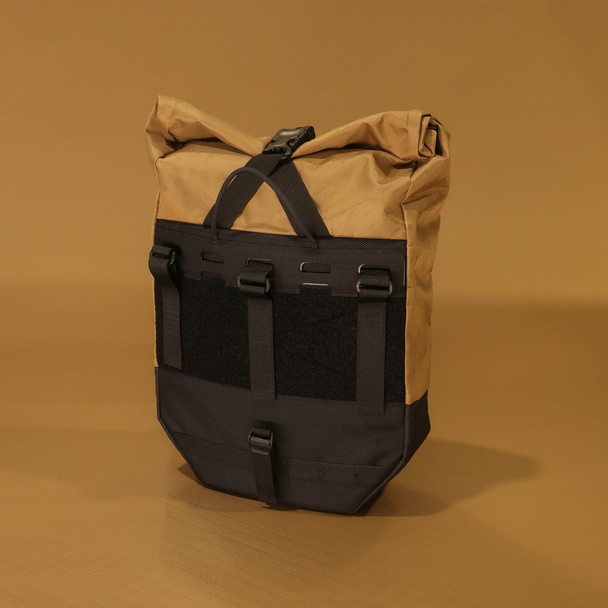 Rear view of 10L roll-top bicycle pannier in coyote tan and black, showing full rack attachment panel with carry handle, hook-and-loop straps, velcro patch, and bottom buckle