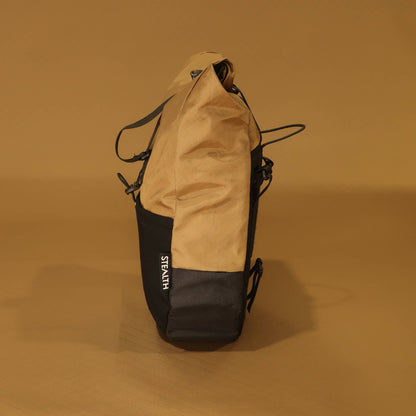 Side profile of 10L Coyote pannier showing tapered shape, coyote tan upper and black lower panels, side zip pocket, and stretch pocket