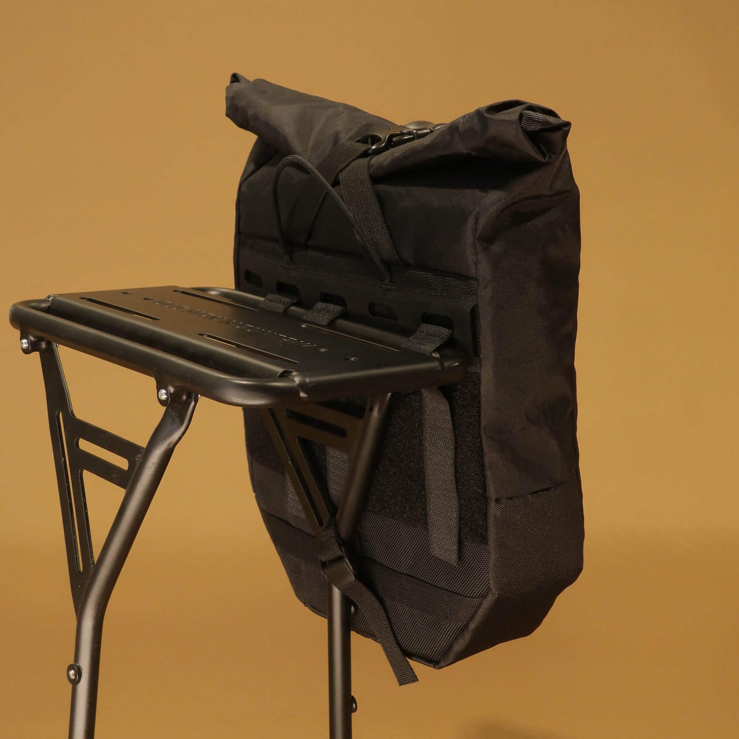 Close-up of 8L black pannier mounted on a rear bike rack, showing the rack attachment strap system from the front angle