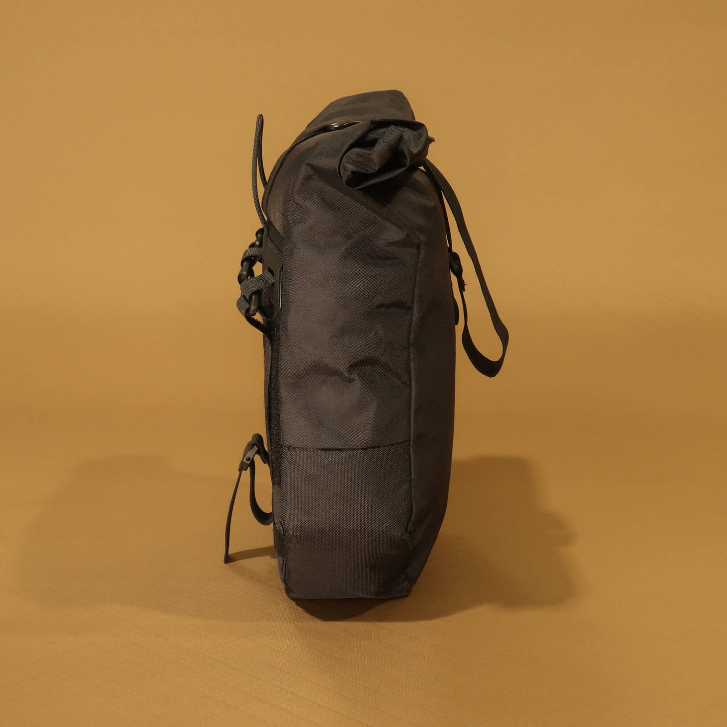 Side profile of black 8L roll-top bicycle pannier showing tapered base and side zip pocket