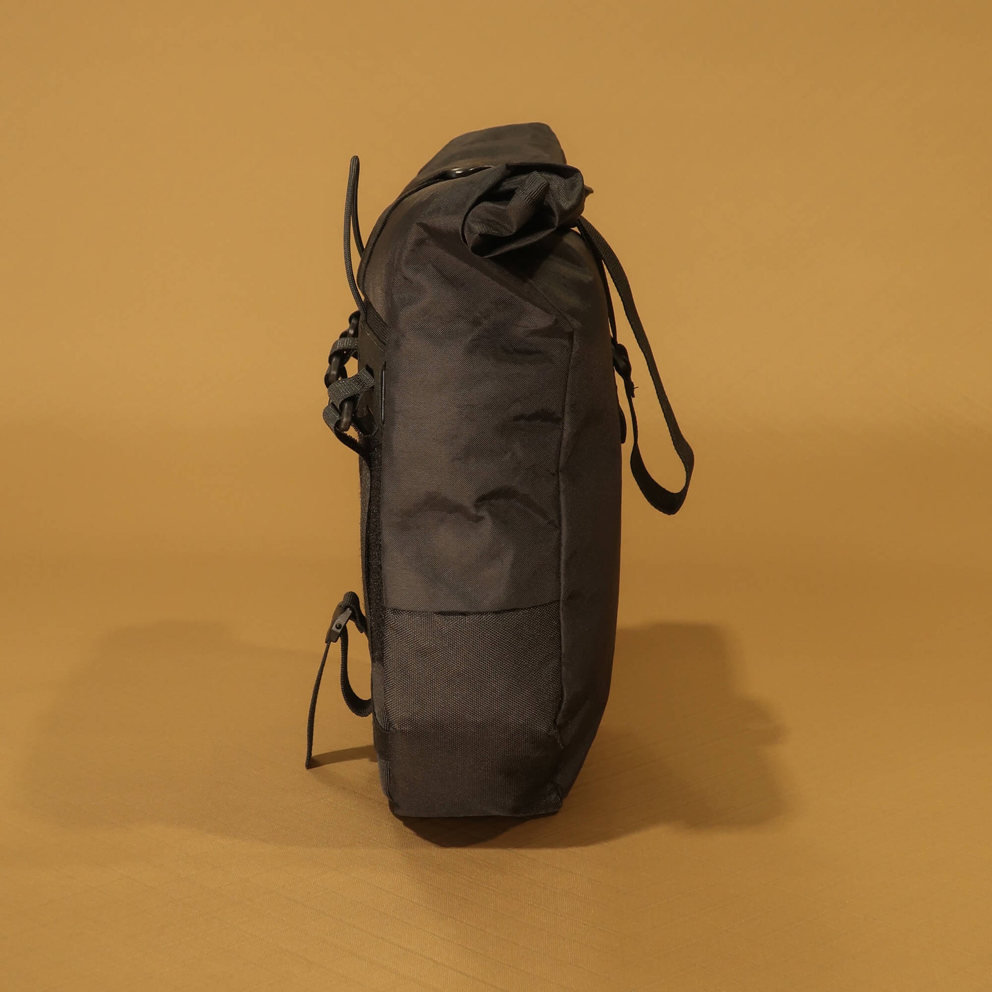 Side profile of black 8L roll-top bicycle pannier showing tapered base and side zip pocket