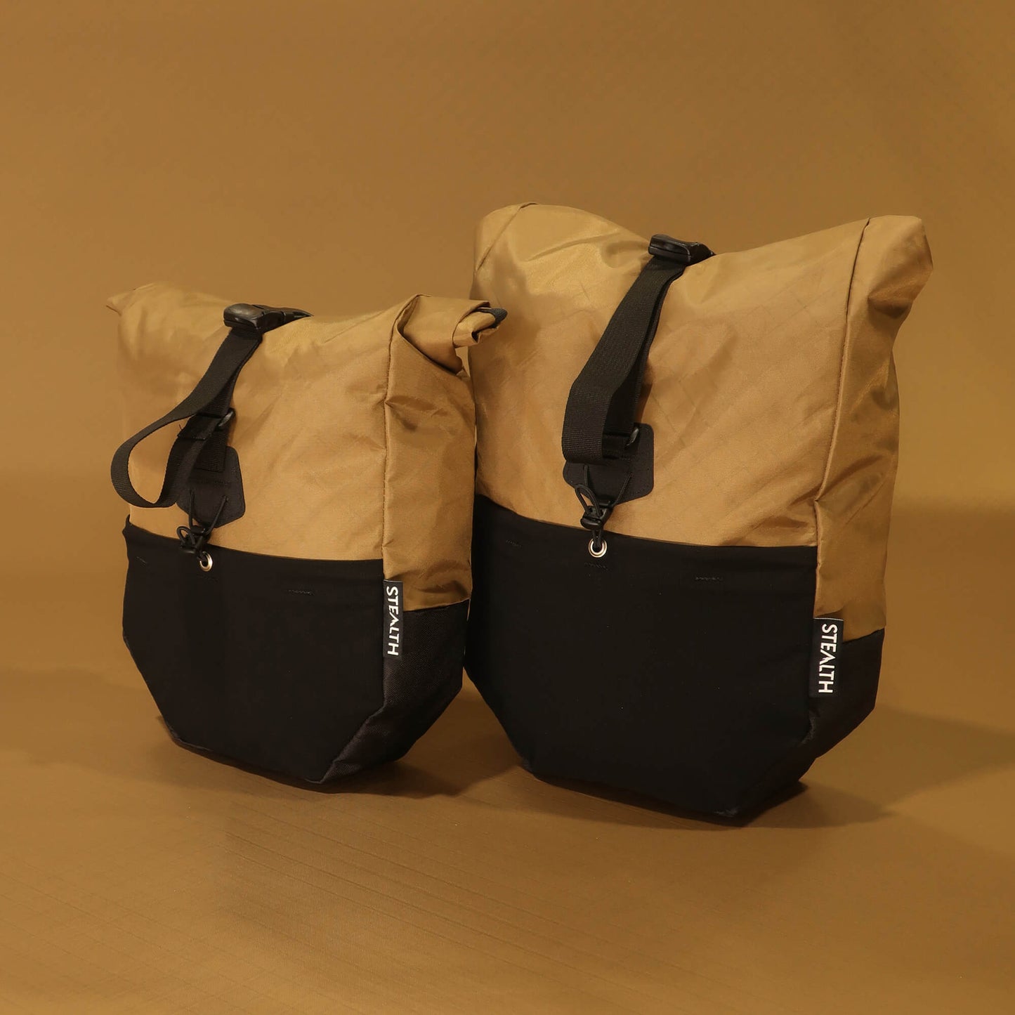 8L and 10L bicycle panniers in coyote tan and black side by side from the front, showing the size difference between the two volumes when fully packed