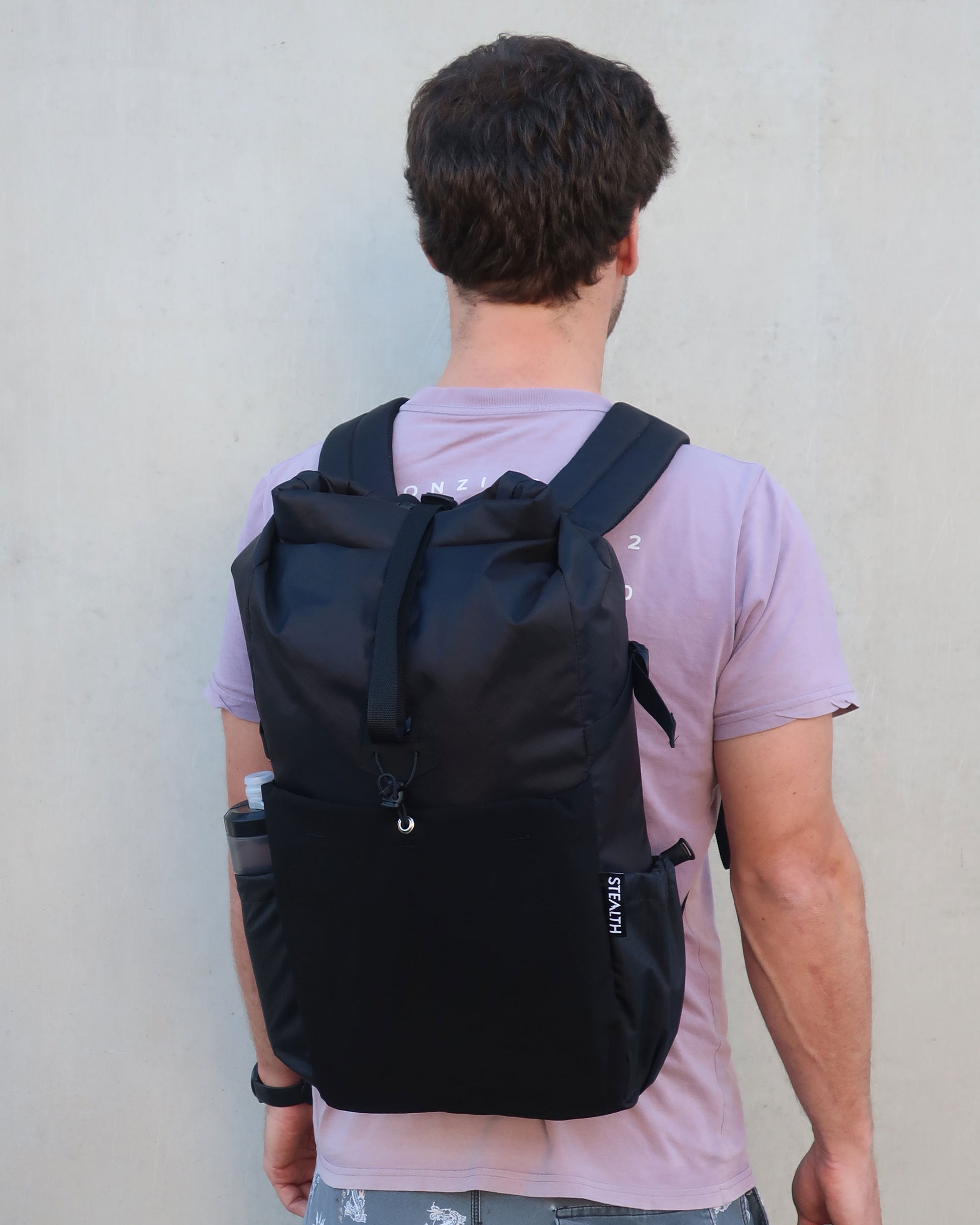 Rata 25 black roll-top backpack worn from behind showing ultragrid bottle pocket in use made by Stealth Wellington NZ