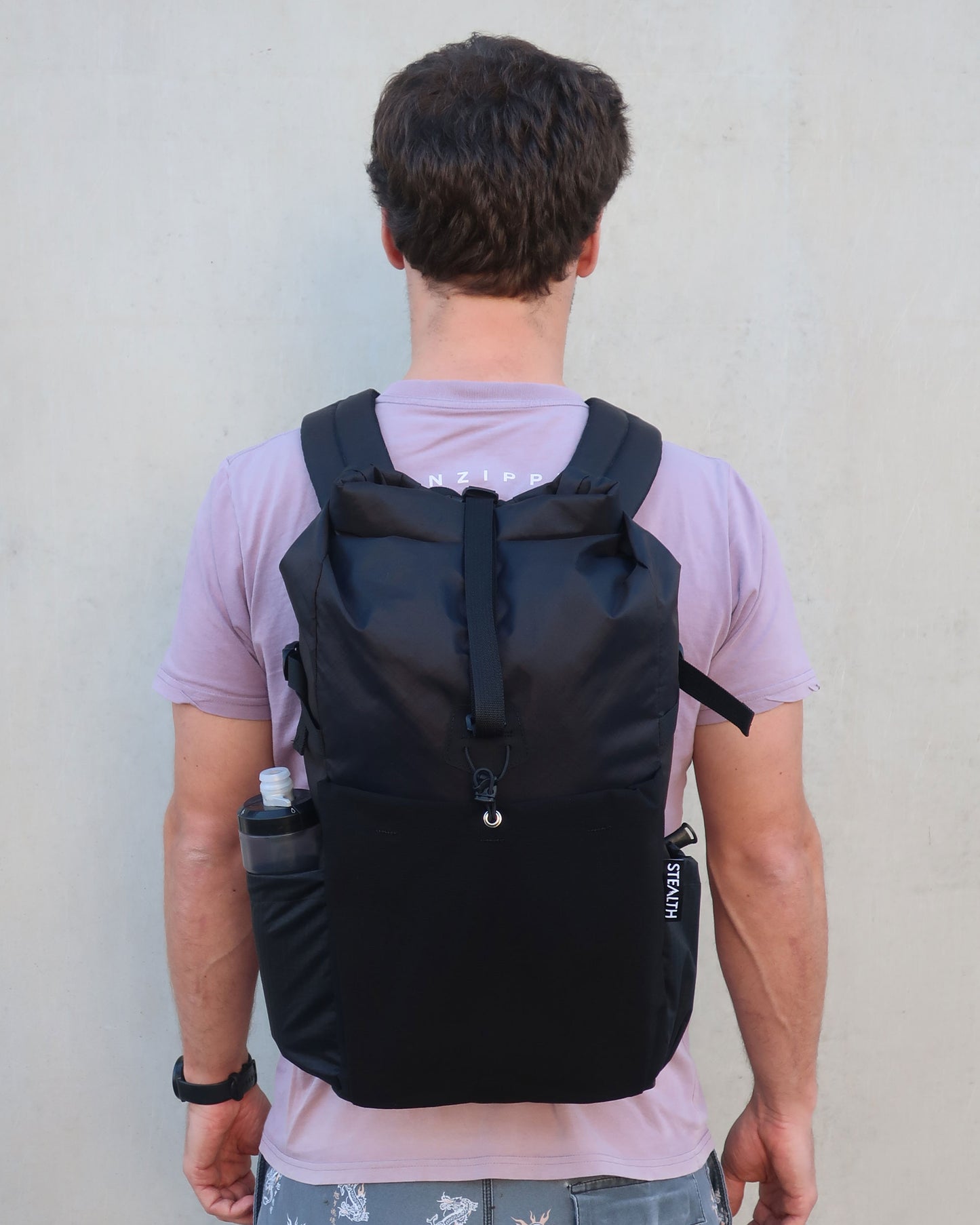 Rata 25 black daypack worn from behind showing full back view and bottle in side pocket made by Stealth Wellington NZ