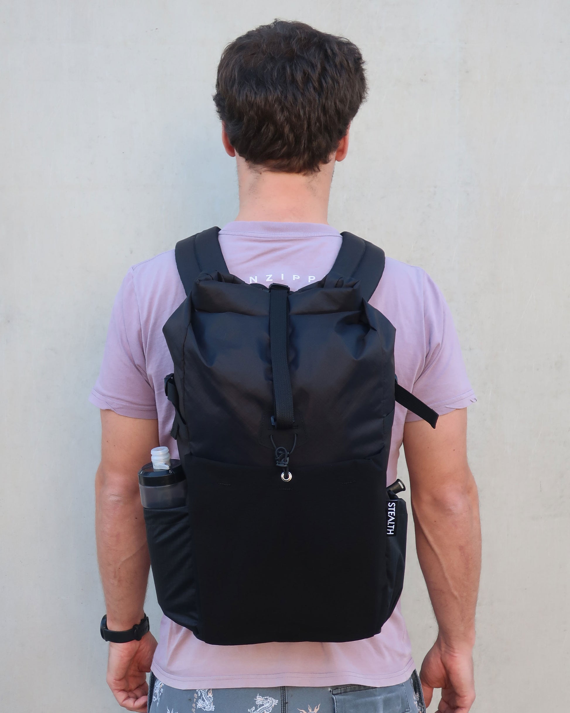 Rata 25 black daypack worn from behind showing full back view and bottle in side pocket made by Stealth Wellington NZ