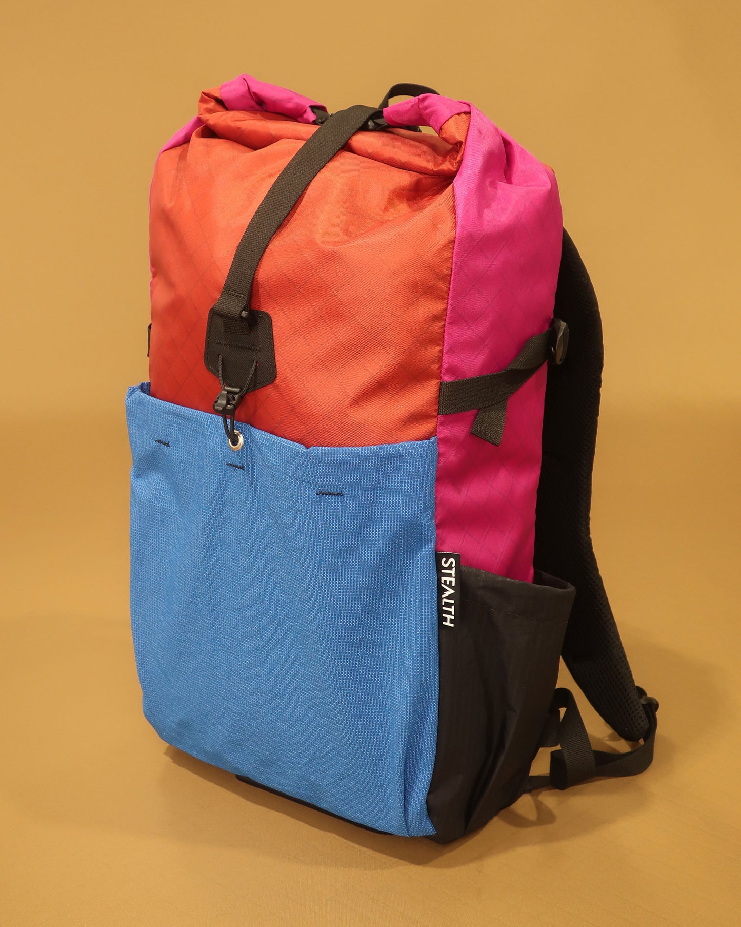 Rata 25 roll-top daypack in brick red fuchsia and blue showing ultrastretch front pocket made by Stealth Wellington NZ
