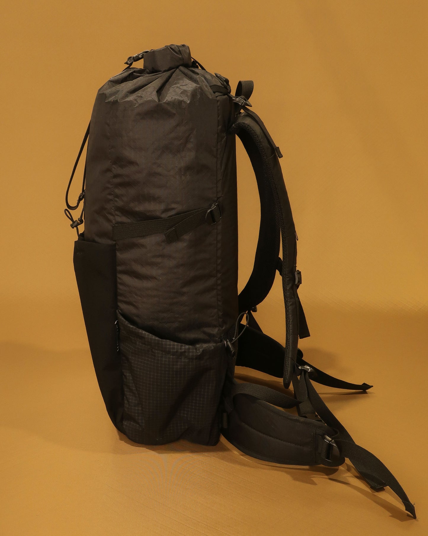 Black 40L tramping pack side profile showing roll-top closure and Ultragrid side pocket, made by Stealth Wellington NZ