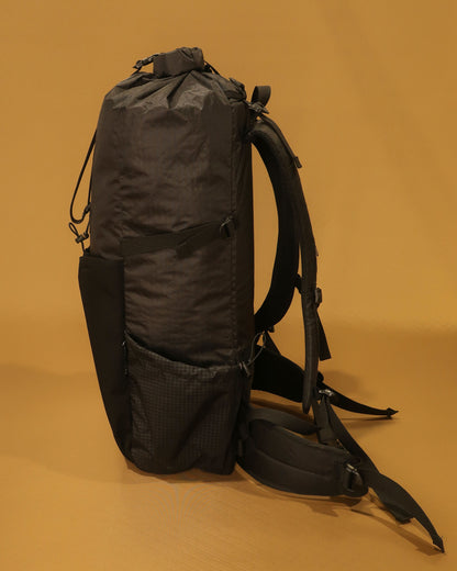 Black 40L tramping pack side profile showing roll-top closure and Ultragrid side pocket, made by Stealth Wellington NZ