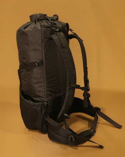 Black 40L tramping pack corner view showing roll-top closure and Ultragrid side pocket, made by Stealth Wellington NZ
