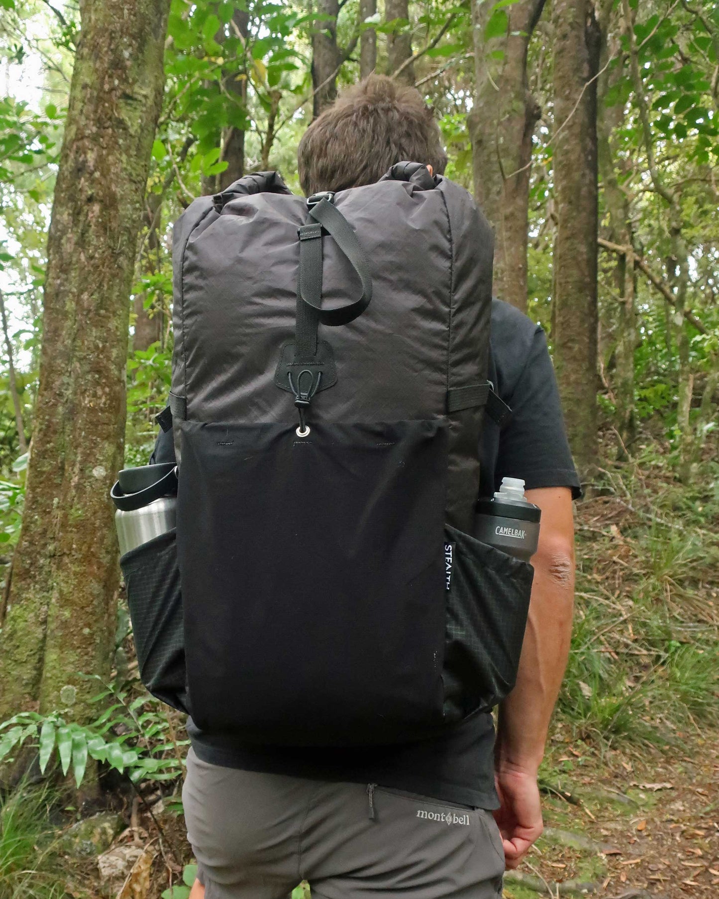 Rata 40 black tramping pack worn on trail in NZ bush, rear view showing loaded side pockets, made by Stealth Wellington NZ