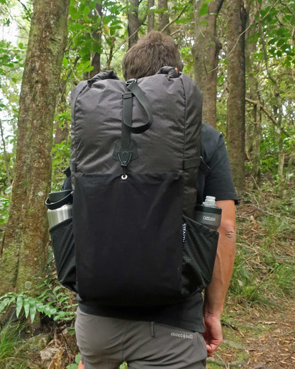 Rata 40 black tramping pack worn on trail in NZ bush, rear view showing loaded side pockets, made by Stealth Wellington NZ