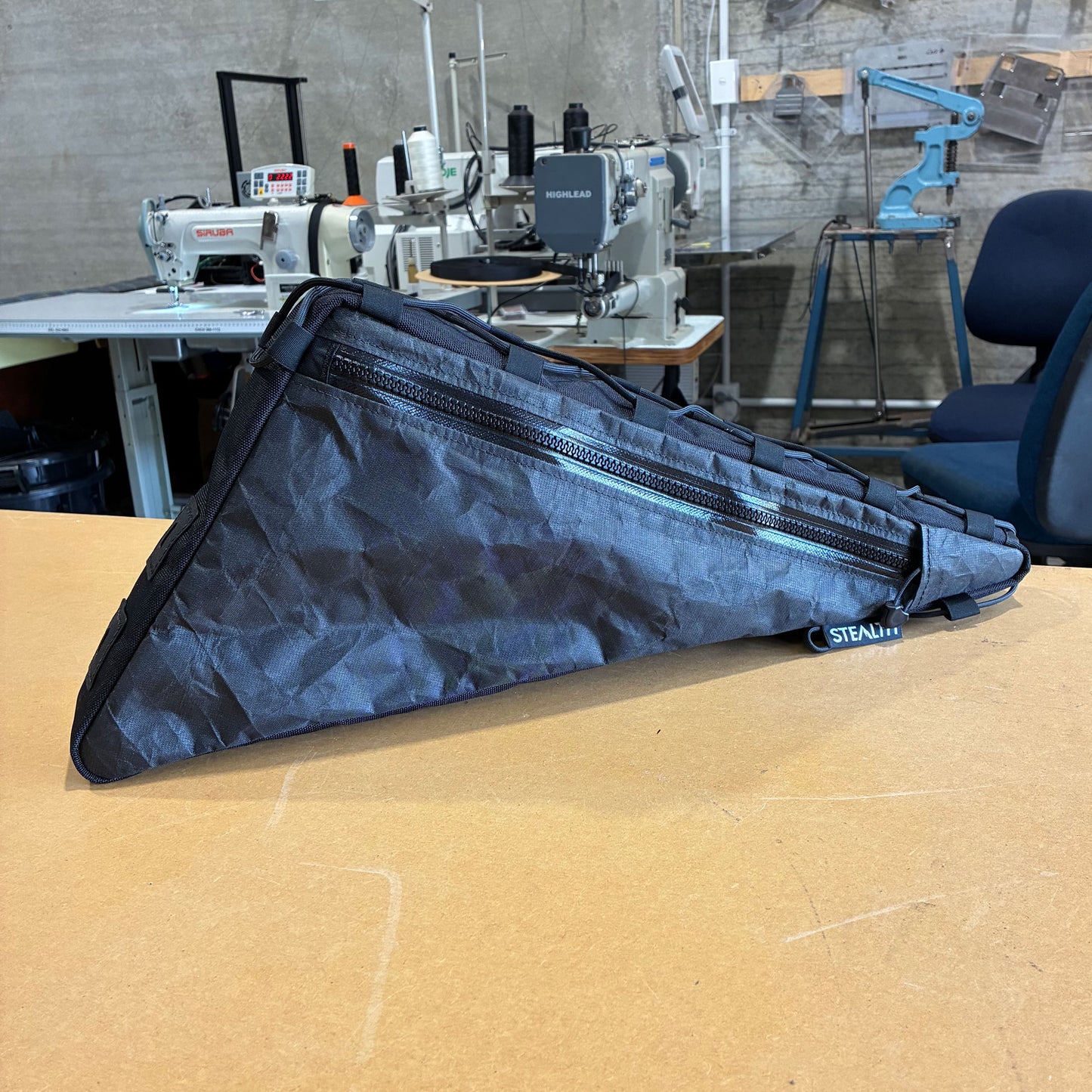 Black handmade bikepacking frame bag with single zip, designed for durable outdoor cycling use, displayed in workshop.